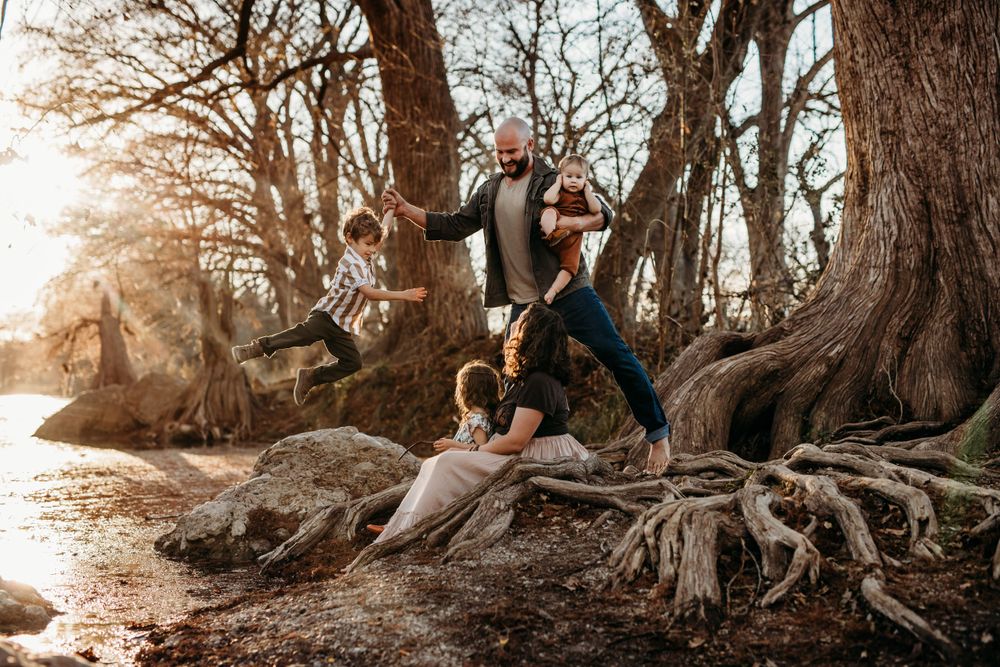family of five playing in the tree roots by the river