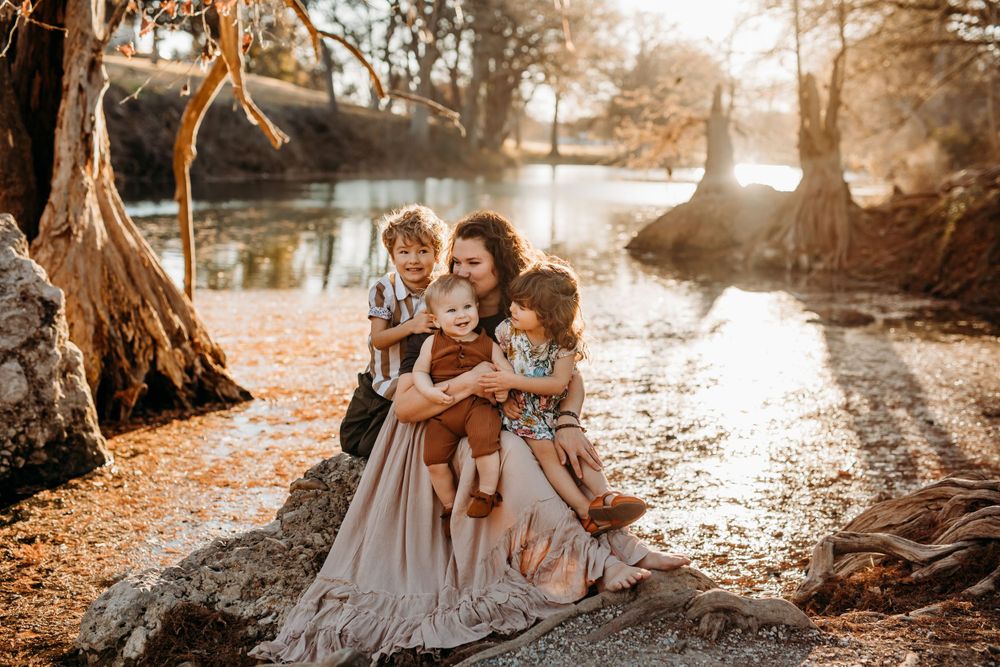 mom with 3 kids sitting on a rock by the water