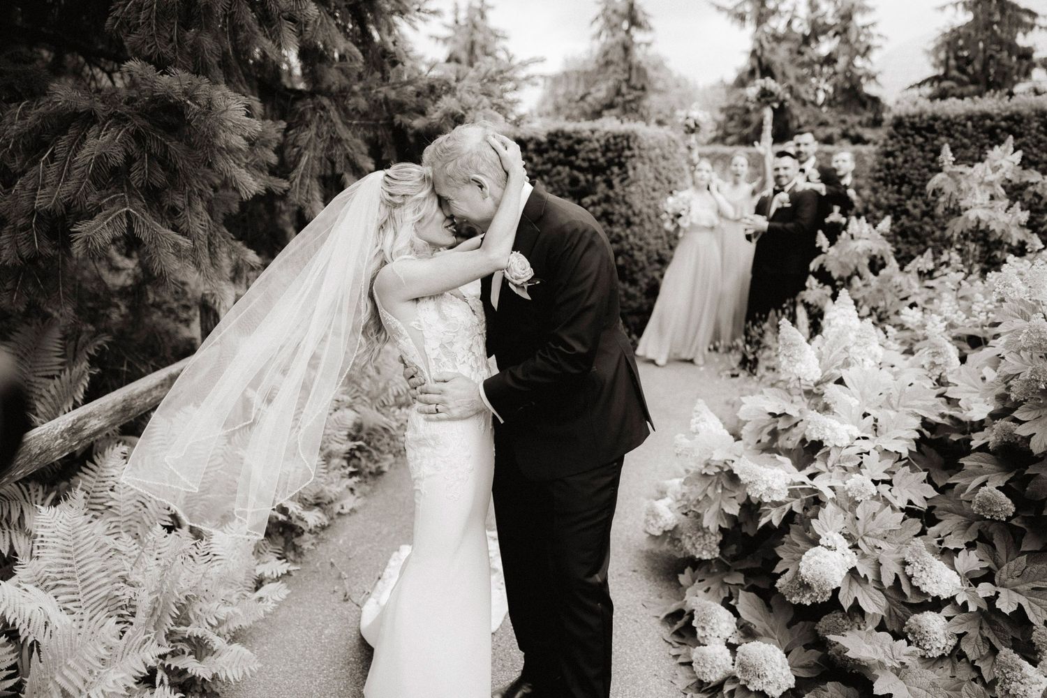 Black and white photo of newlyweds sharing an intimate moment among garden florals.