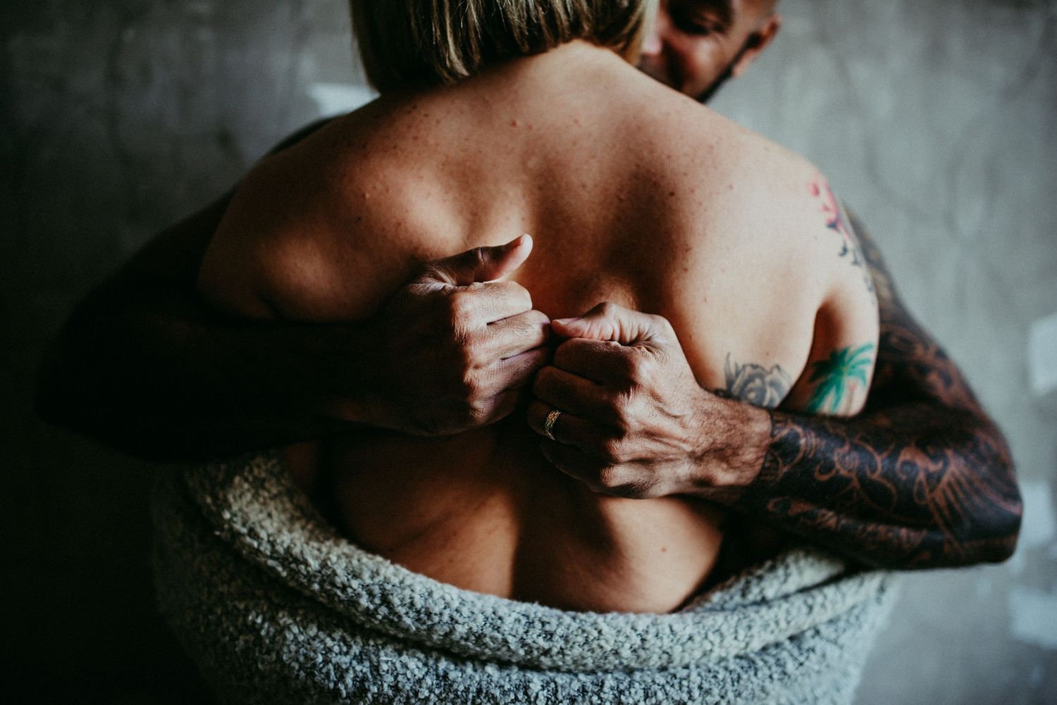Artistic boudoir photo showing tattooed arm and bare back against moody grey background.
