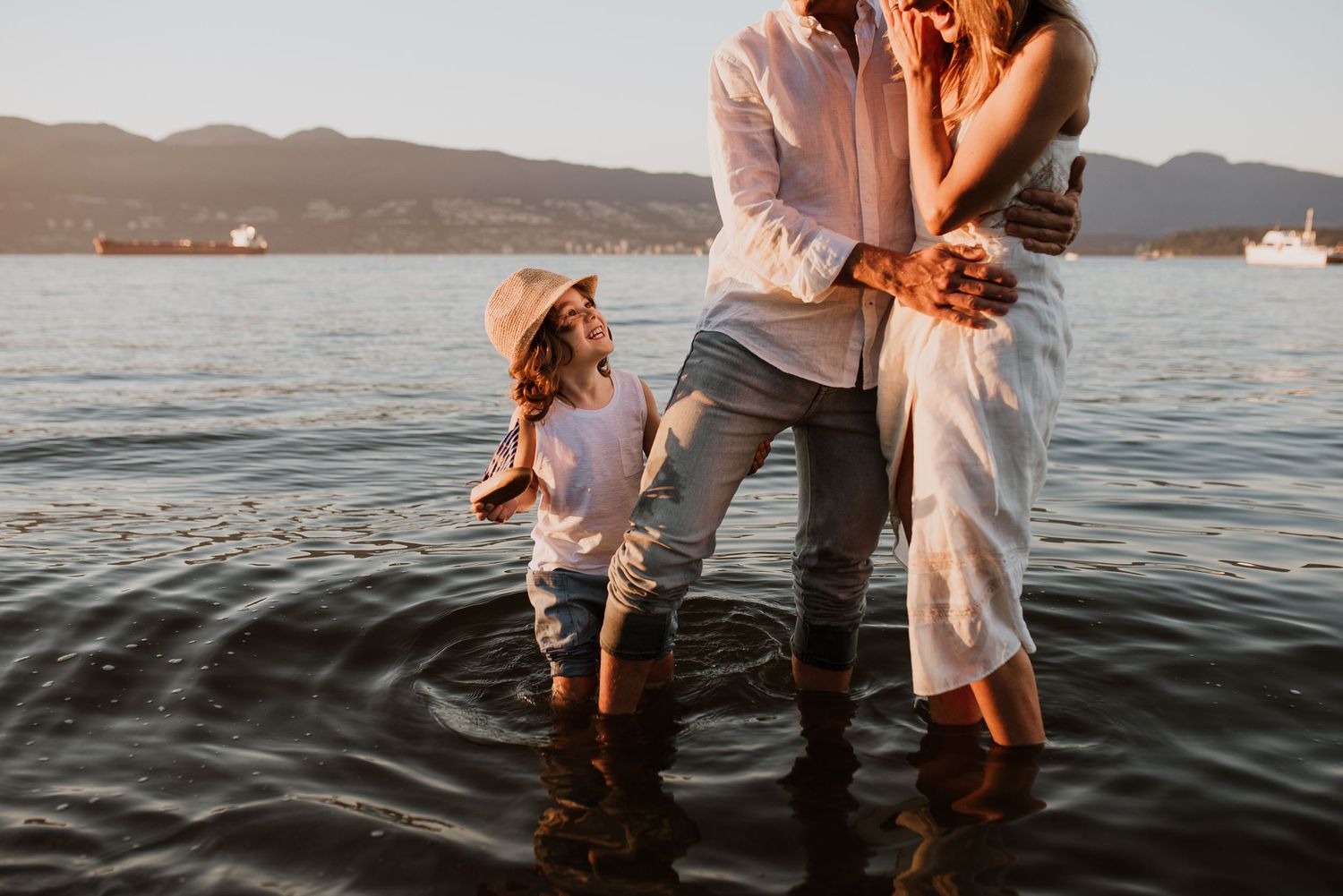 Family of three standing in ocean at sunset at Jericho Beach.