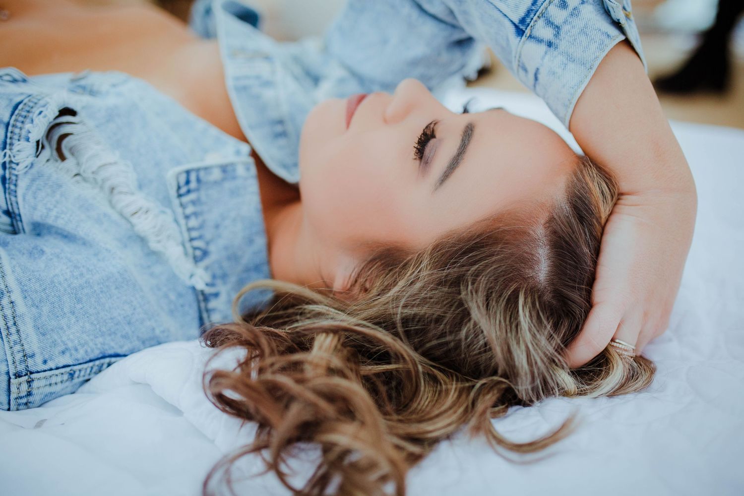 Casual lifestyle portrait of a person lying down in denim clothing with wavy hair spread out.