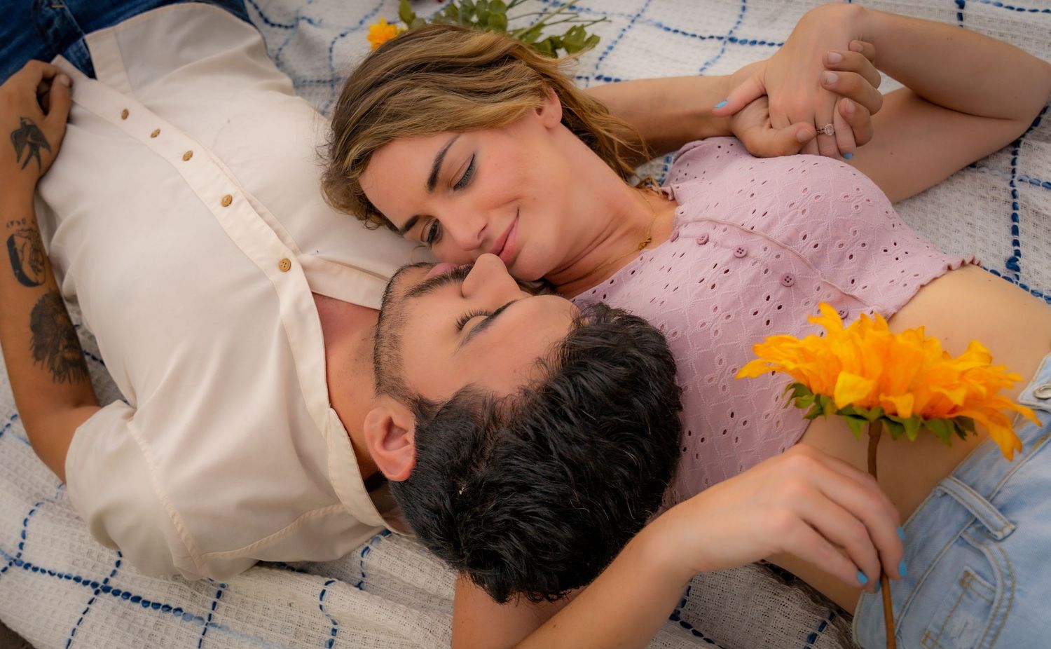 A romantic couple lying together on a blanket with orange flowers in a peaceful outdoor setting.