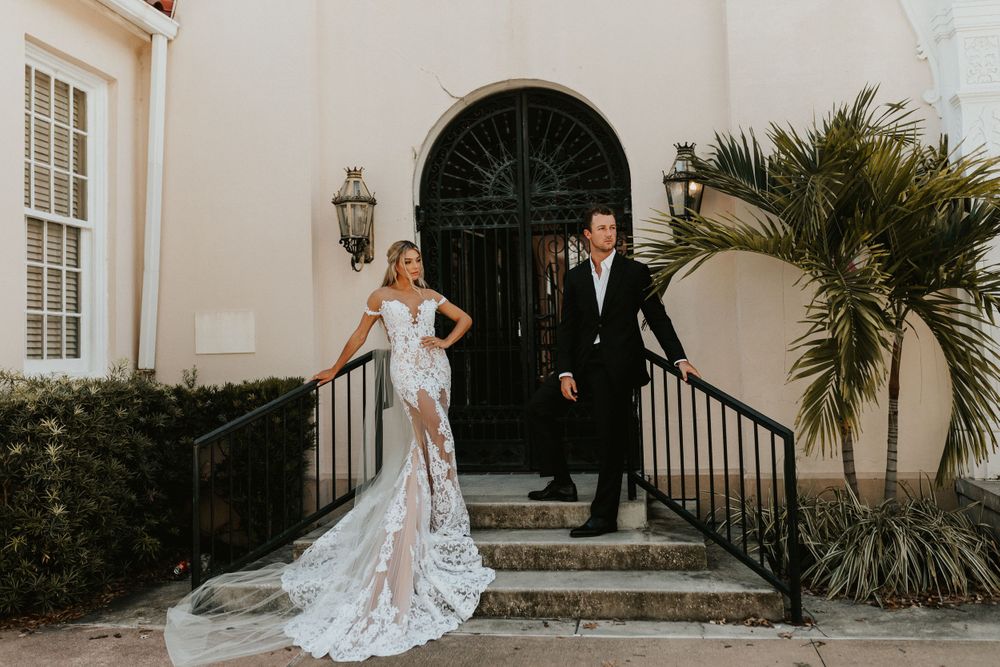 Wedding couple posing on elegant stone steps with palm trees and arched doorway.