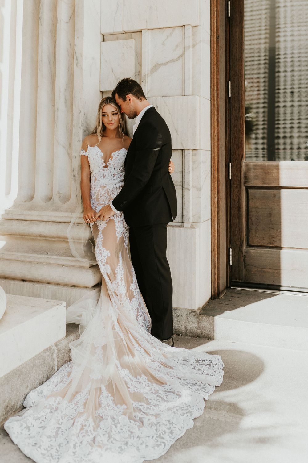 Wedding couple pose intimately against classic white columns in elegant bridal attire.