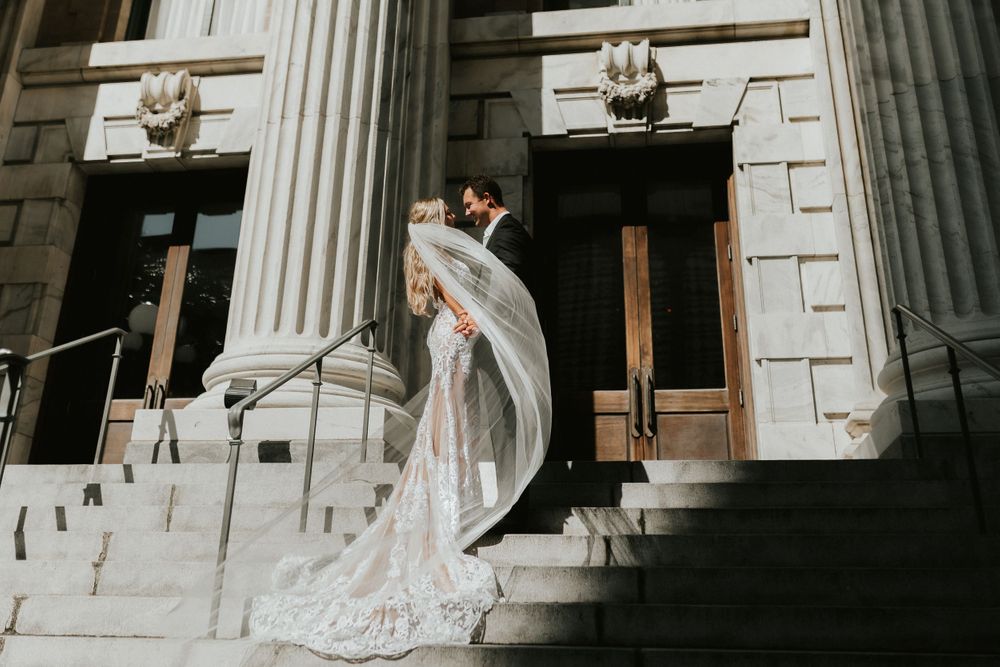 Dramatic wedding pose on grand stone steps with bride's dress flowing in the wind.