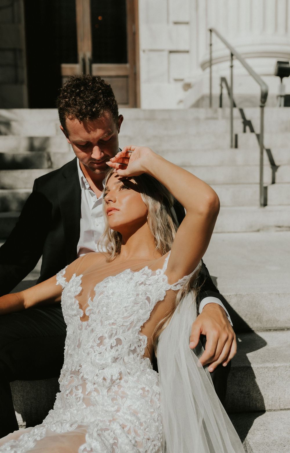 Intimate sunlit wedding portrait on stone steps with delicate lace details.