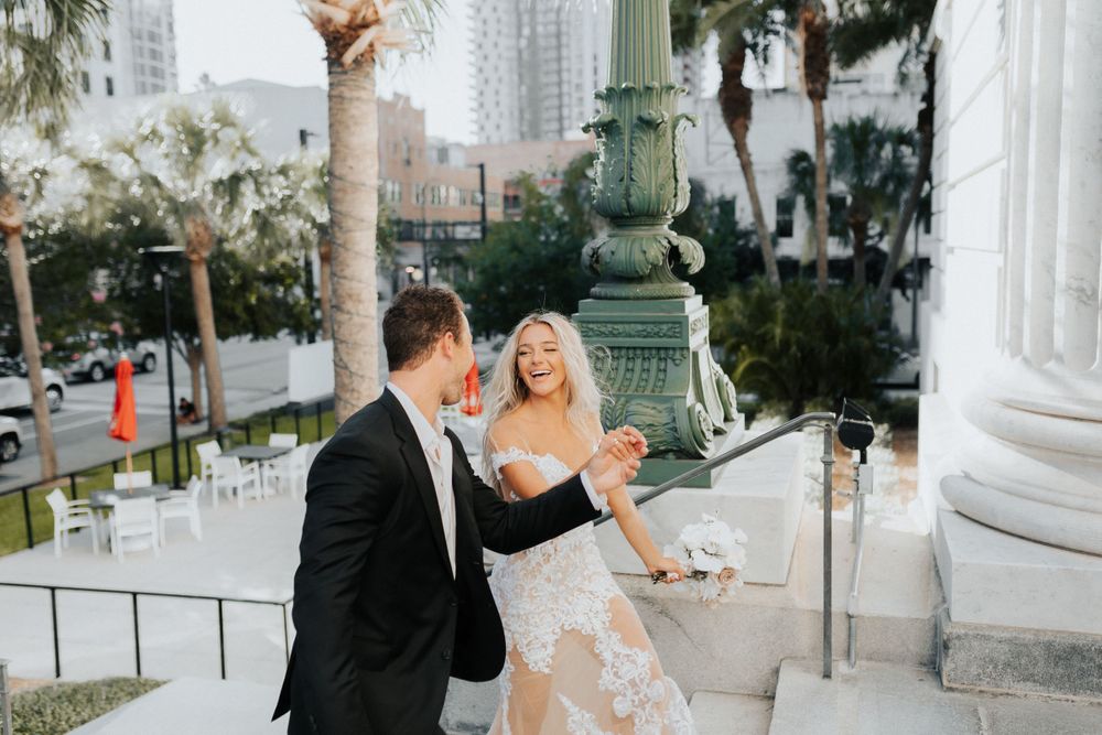 Elegant couple laughing together near ornate white pillars and palm trees.