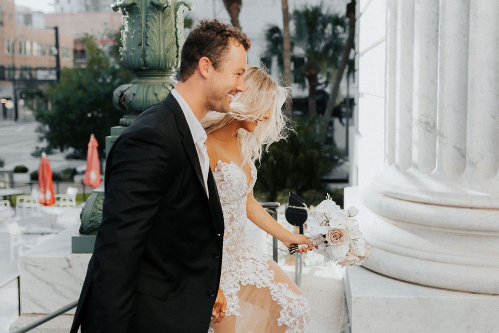 A tender wedding moment captured beside white marble columns and palm trees.