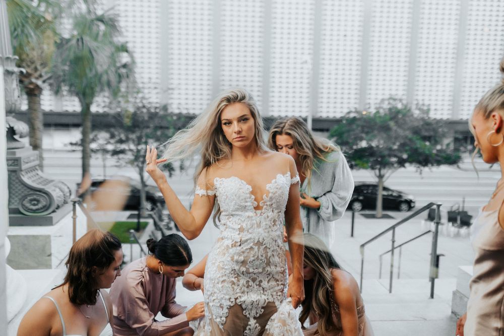 Bride in detailed lace wedding dress surrounded by guests on outdoor steps.