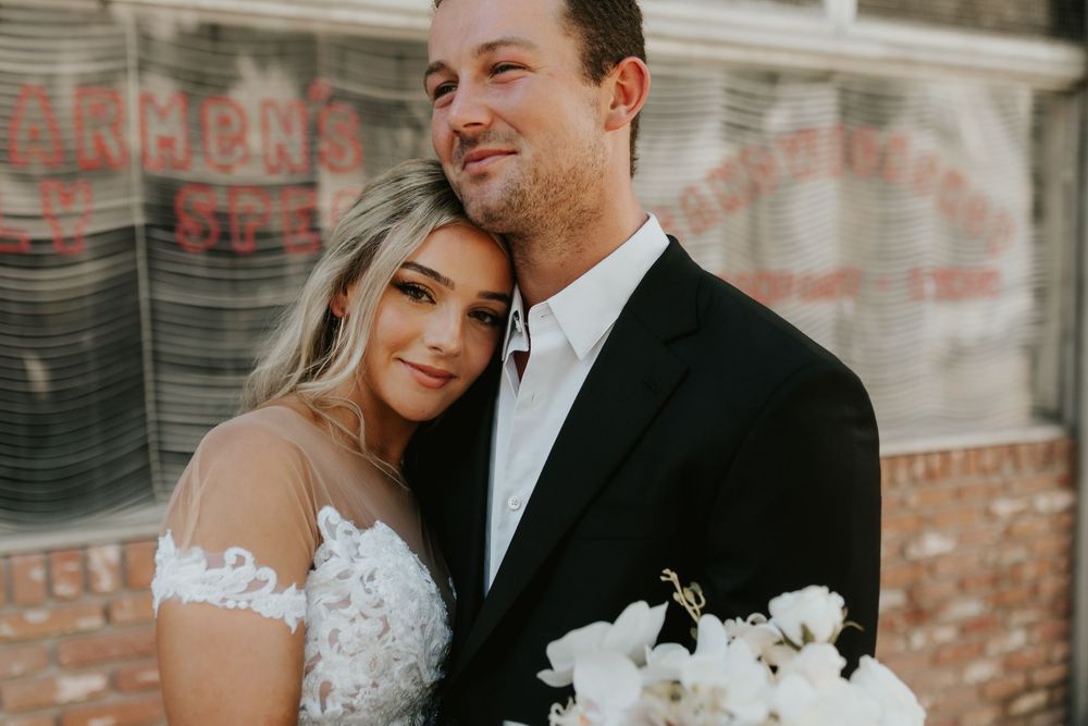 Romantic wedding portrait against brick wall with white floral bouquet.