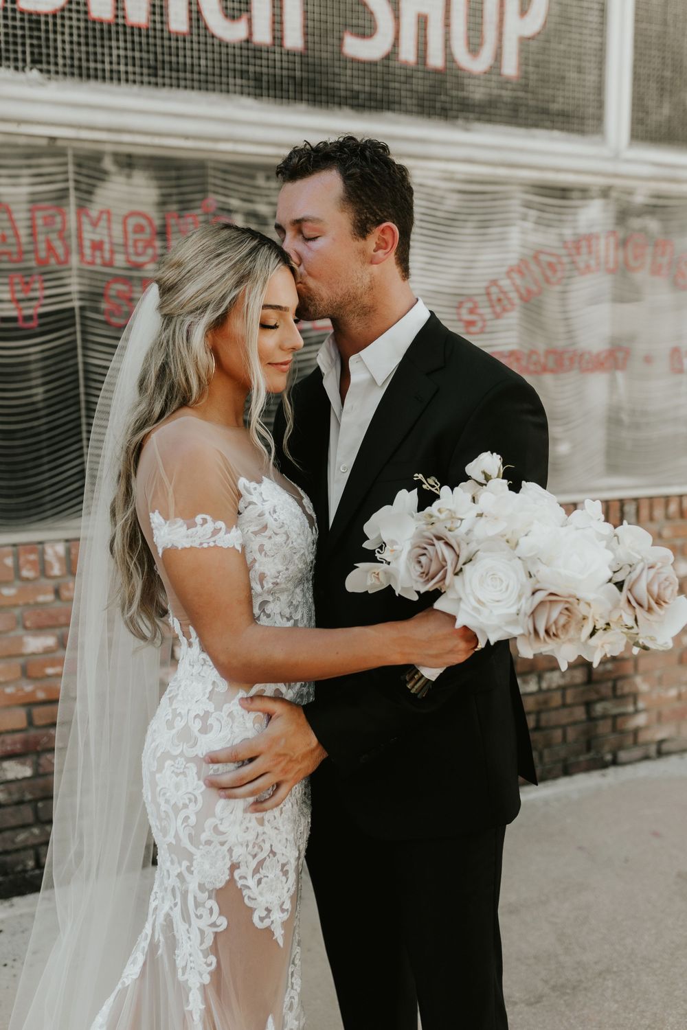 Romantic wedding portrait with white rose bouquet against vintage storefront.