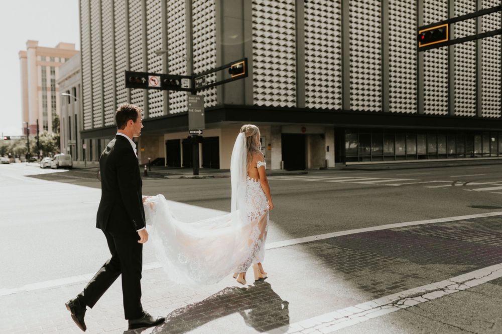 Wedding couple walking through urban setting with flowing lace dress and veil.