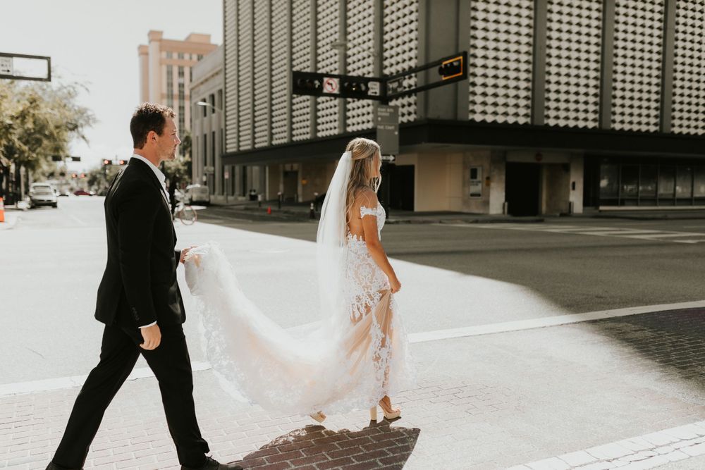 Newlyweds walk down urban street with flowing white wedding dress and veil.