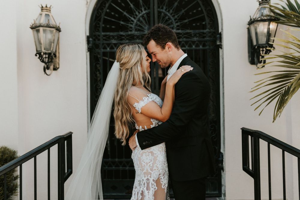 Romantic wedding portrait in front of ornate doorway with decorative lanterns.