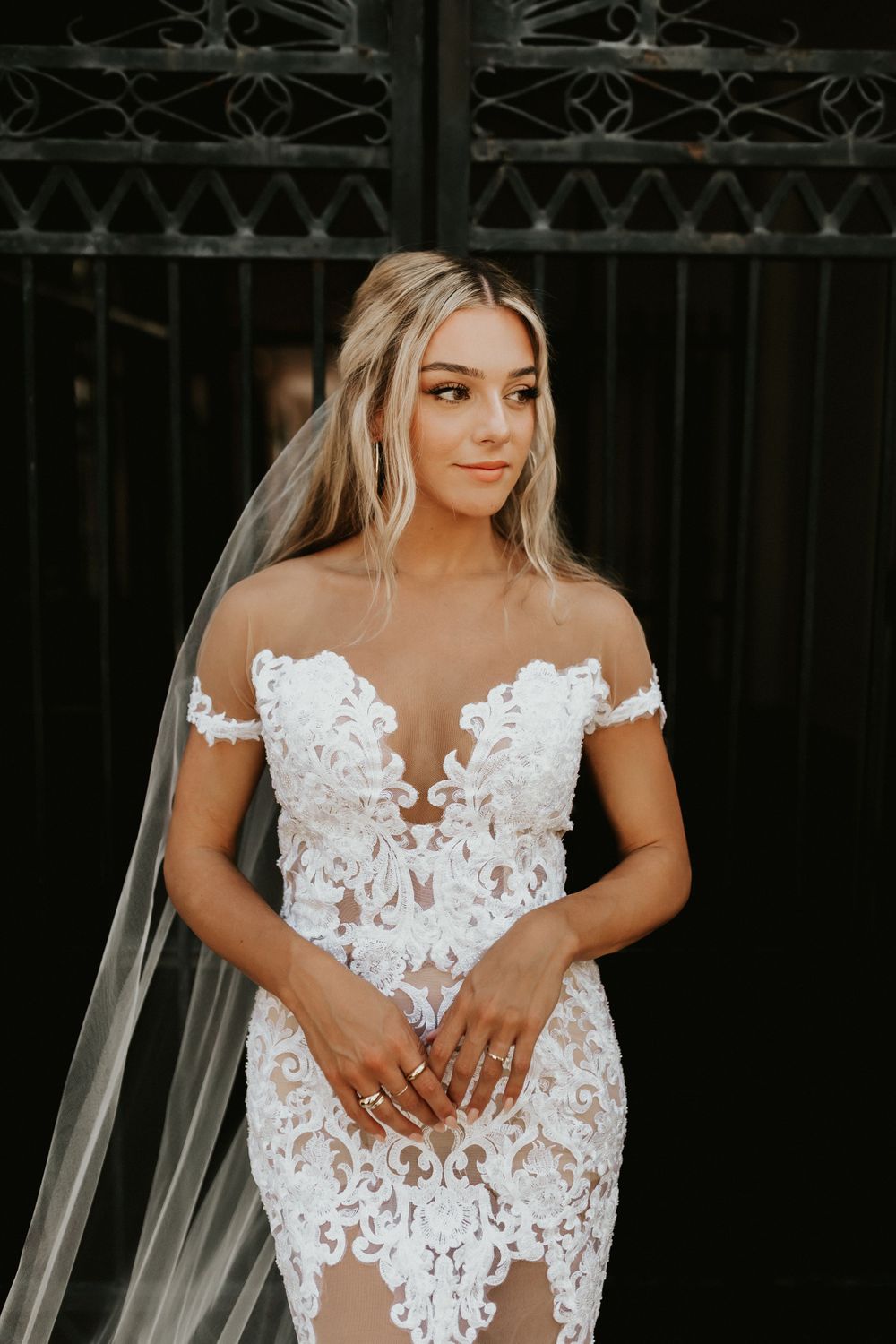 Elegant off-shoulder wedding dress with intricate lace details and sheer elements.