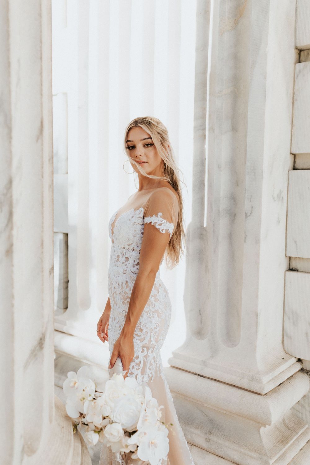 Elegant bridal portrait with white orchid bouquet against classical architecture.