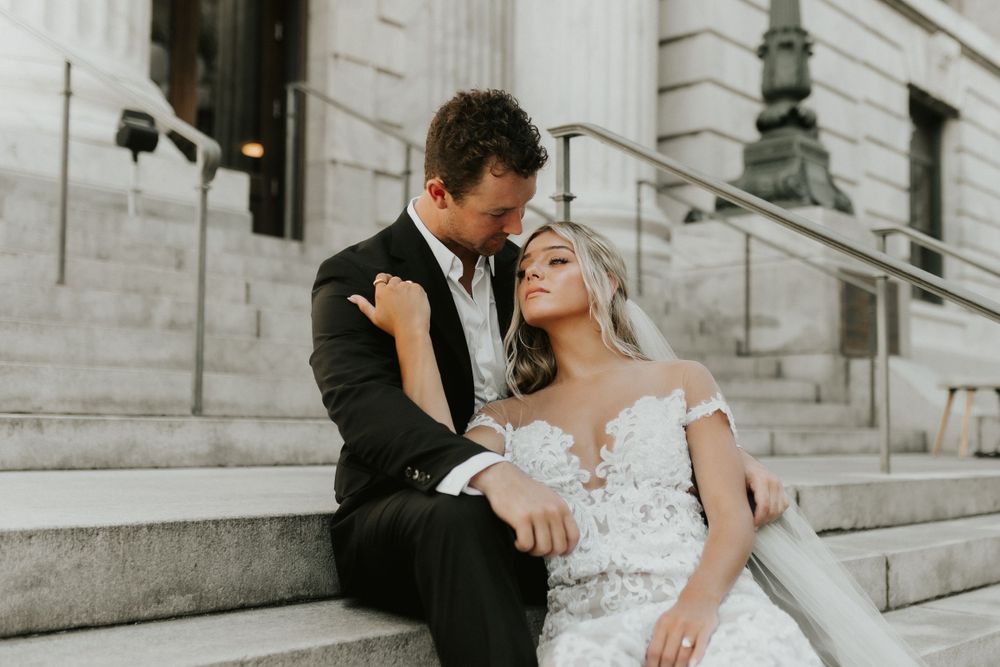 Newlywed couple laughing together while seated on grand stone staircase.