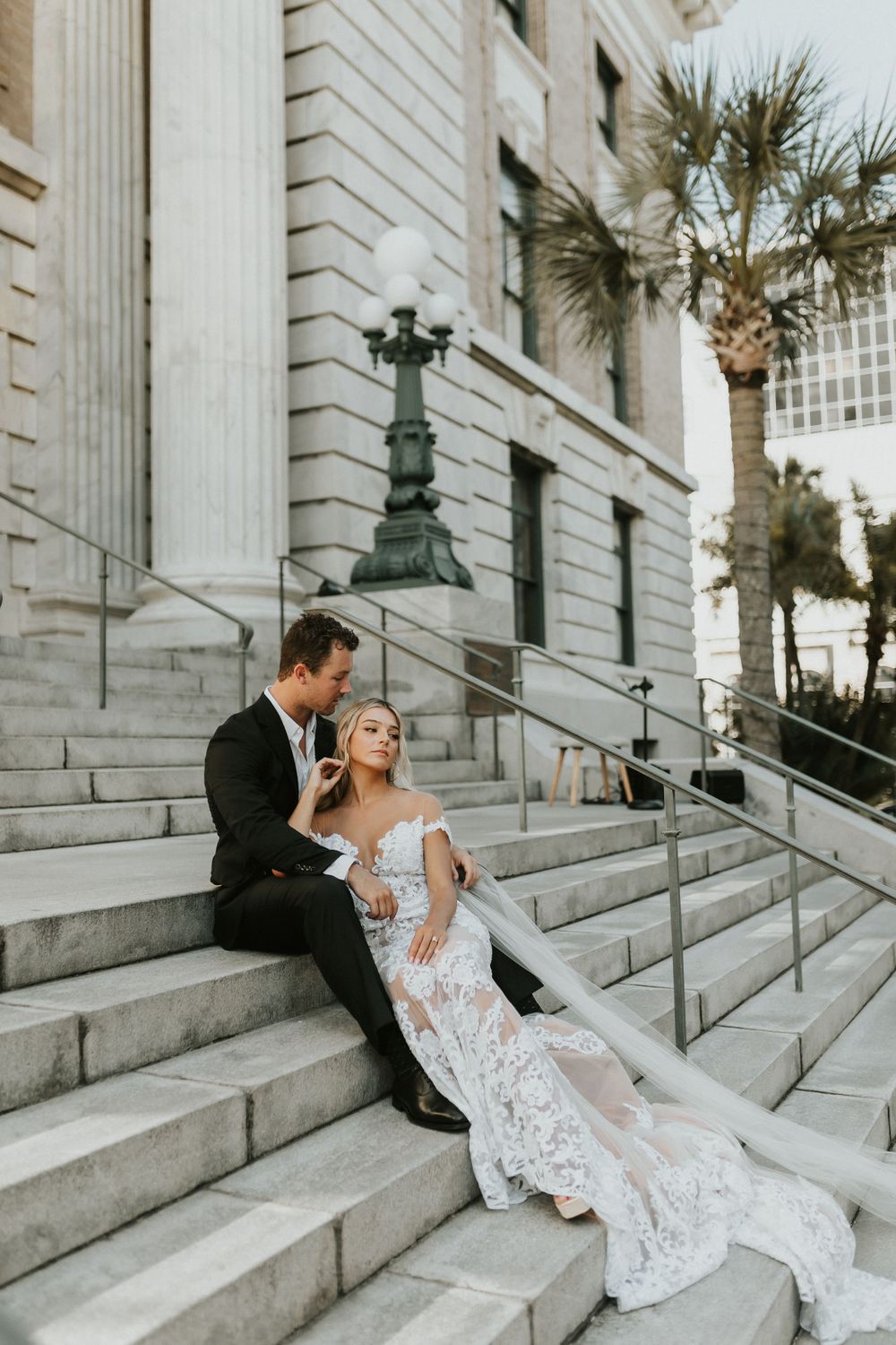Wedding couple poses on historic building steps with palm trees in background.