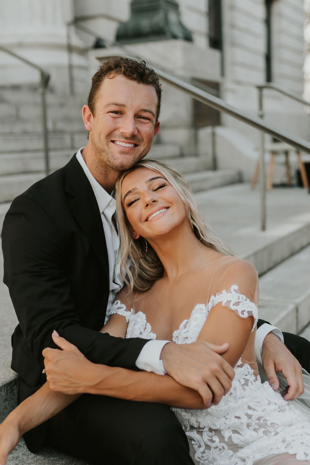 Happy wedding couple embraces while sitting on stone steps outdoors.