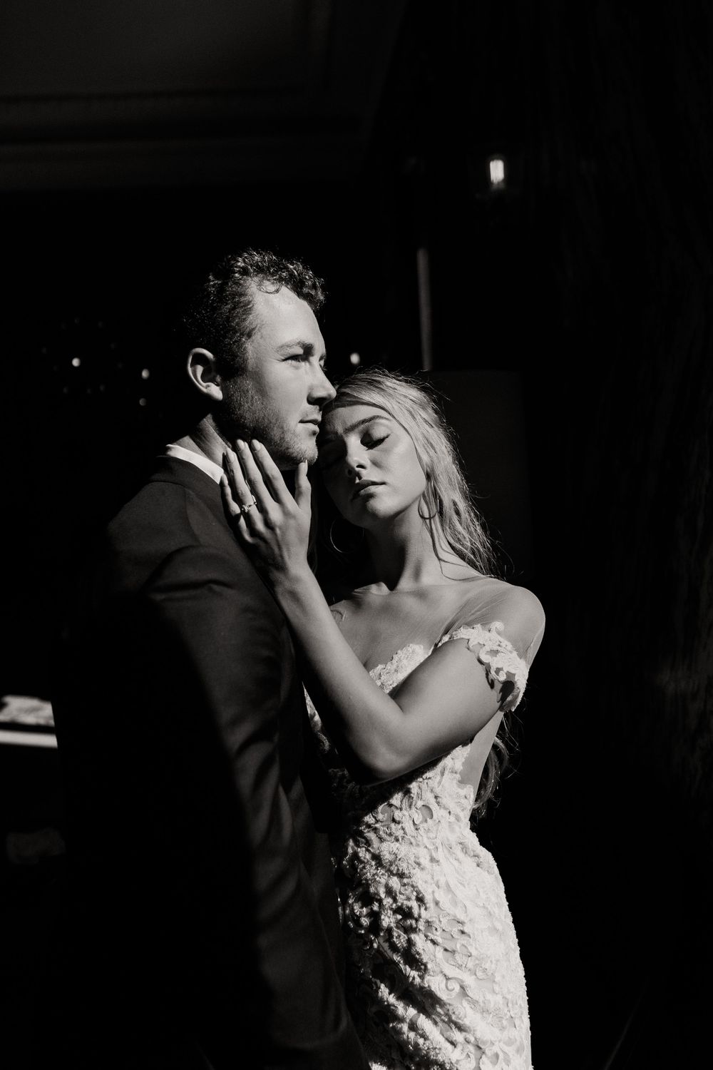 Dramatic black and white photo of couple in wedding attire embracing.