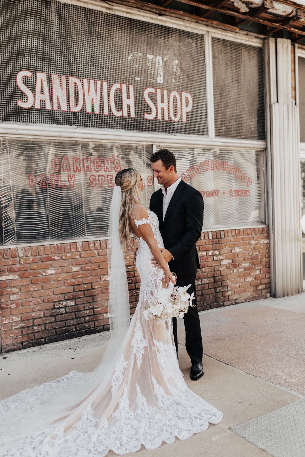 A romantic wedding portrait in front of an old sandwich shop with rustic brick walls.