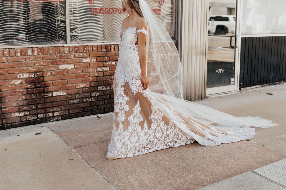 A detailed view of an elegant lace wedding dress train and veil against a brick wall background.