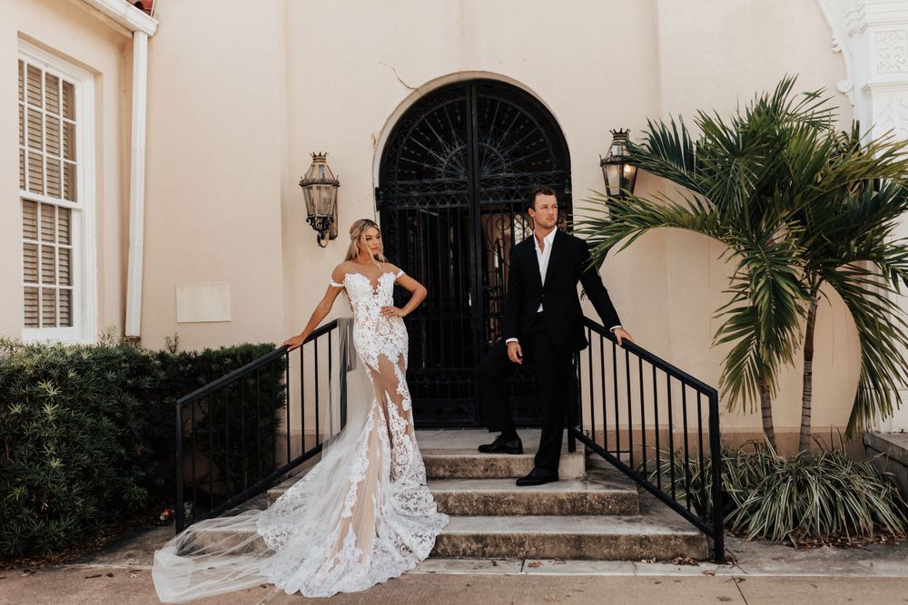 Stylish wedding couple poses on stone steps with elegant archway and tropical greenery.