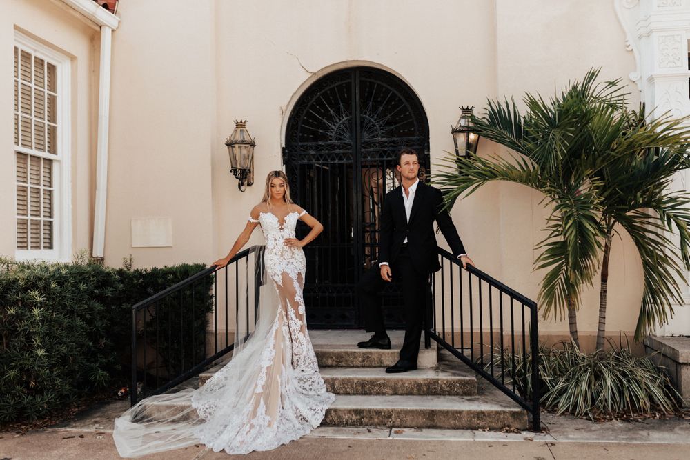 Wedding portrait of couple standing on stone steps with a black arched doorway and palm decor.