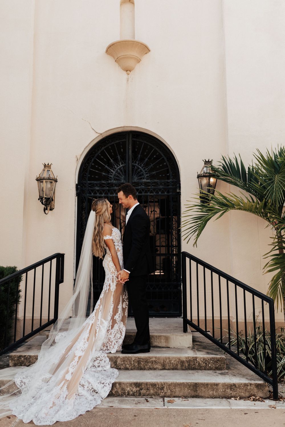 Romantic wedding portrait on stone steps with bride in lace gown and groom in black suit.