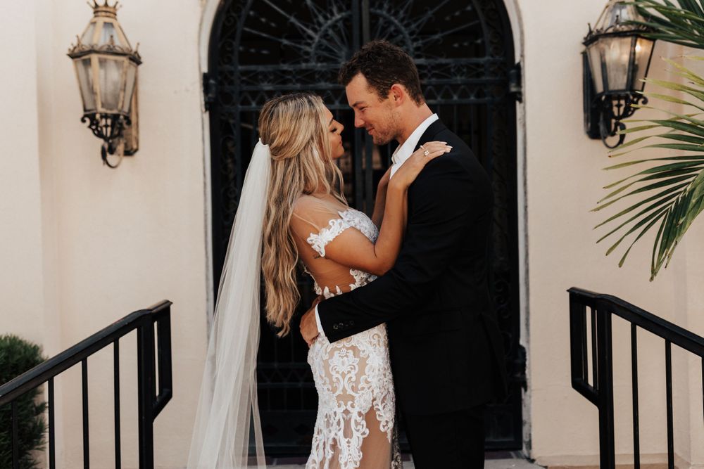 Intimate wedding moment captured on stone steps with ornate black door and lanterns.