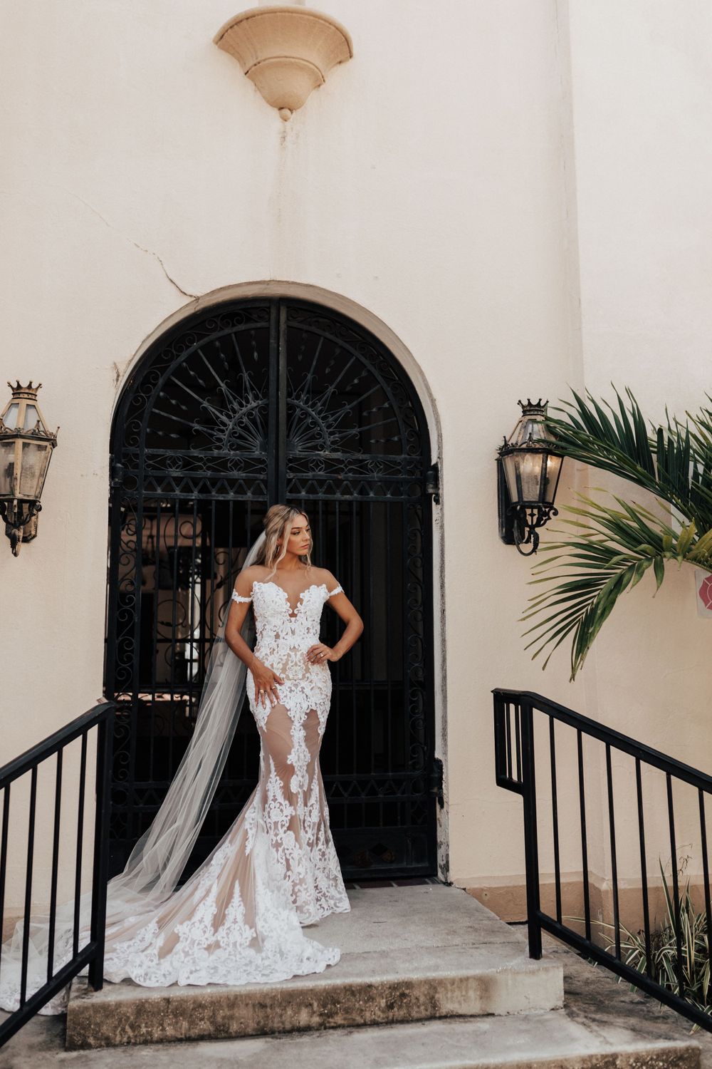 Stunning lace wedding dress with flowing train photographed on church steps with wrought iron details.