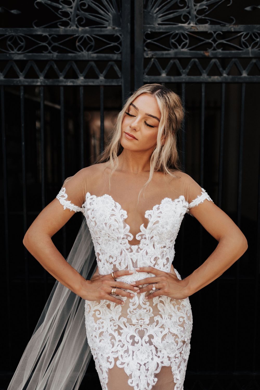 Bridal portrait showcasing delicate lace dress details against ornate iron gate background.