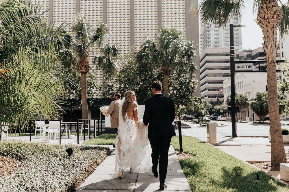Wedding couple walking along palm tree lined path in urban setting.