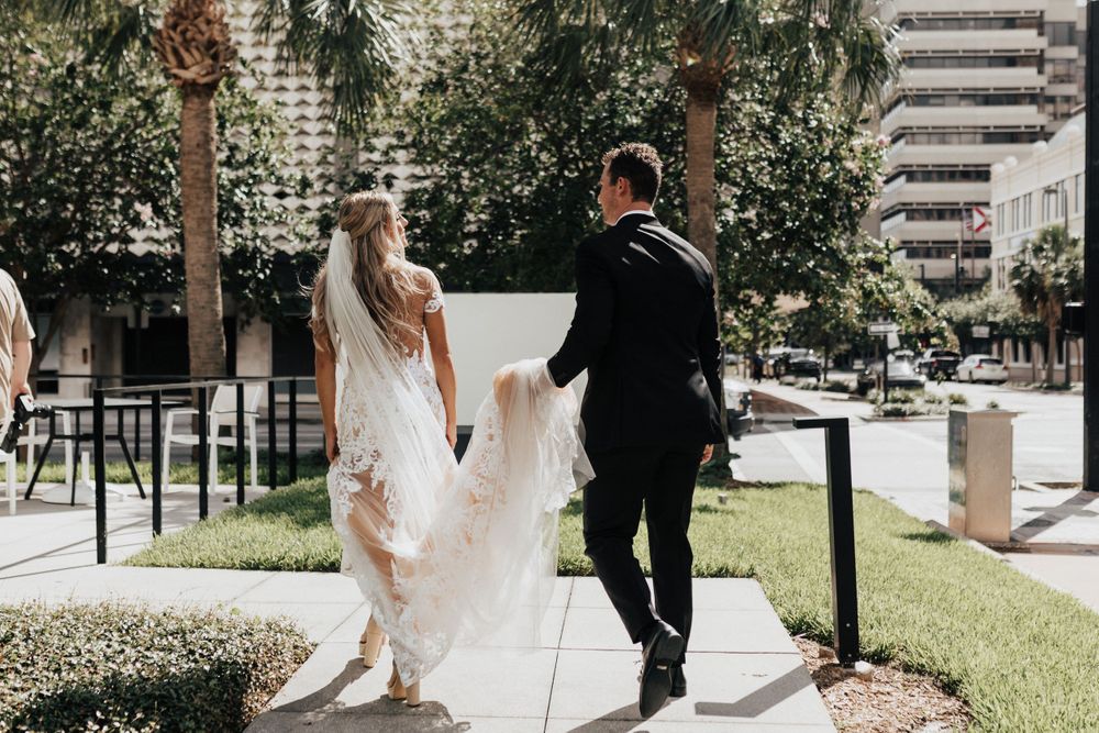Candid wedding photo of couple walking together on urban sidewalk lined with palm trees.