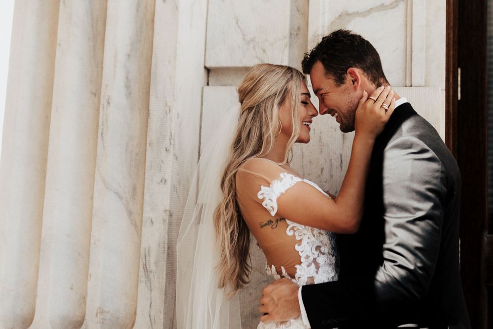 Close-up wedding portrait showing tender moment between couple against white marble backdrop.