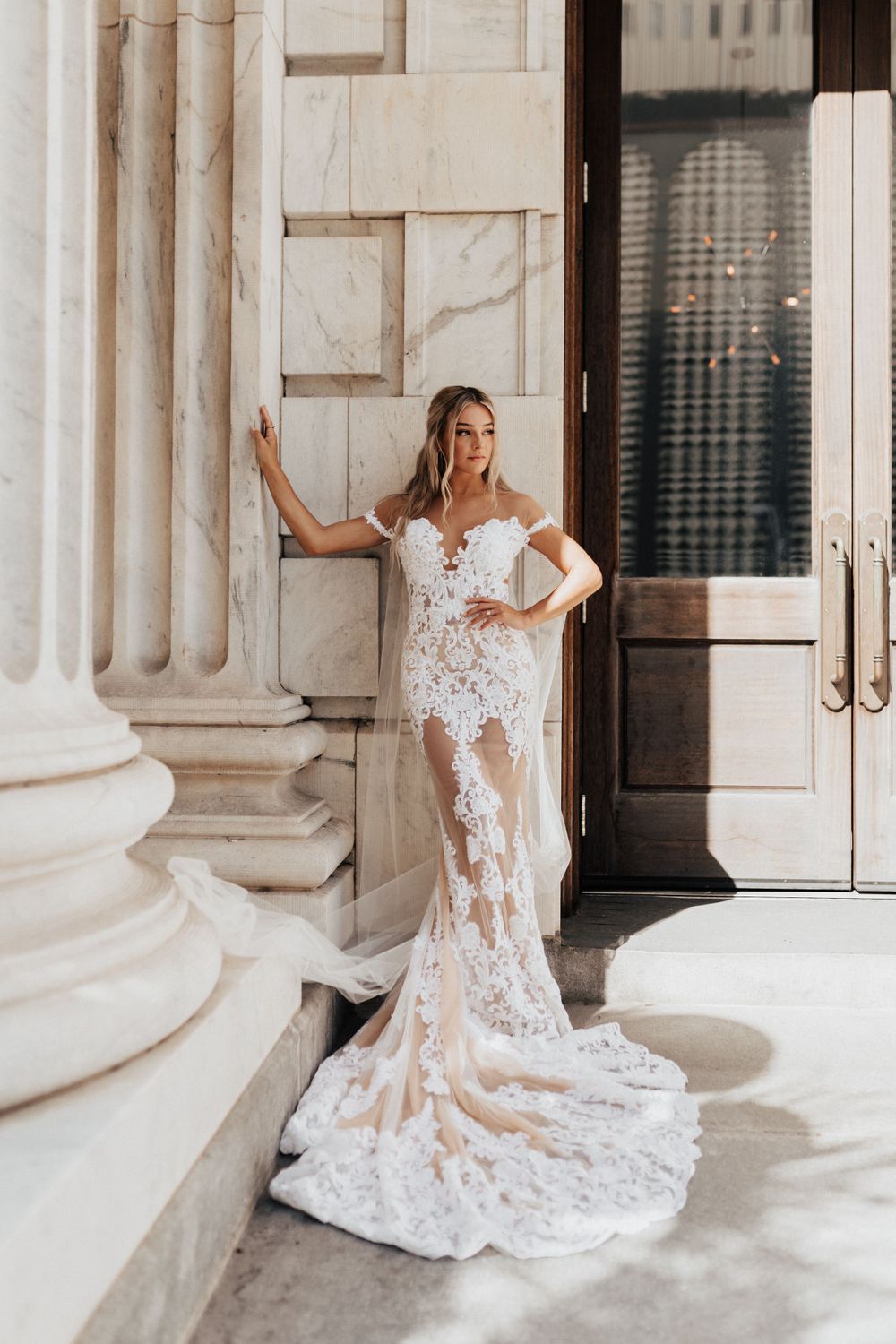 Elegant bridal portrait showcasing detailed lace wedding gown with cathedral train against classic columns.