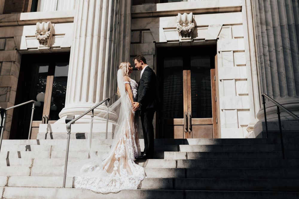 Romantic wedding portrait on stone steps with classical architecture and flowing white dress.