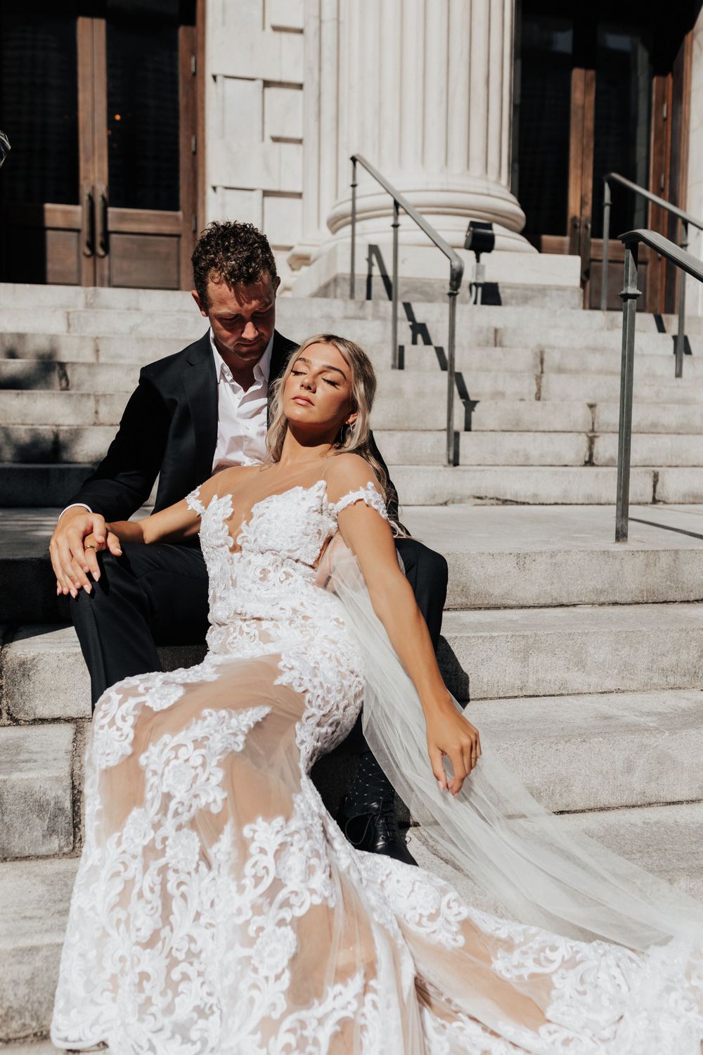 Intimate wedding moment captured on stone steps with dramatic lace gown details.