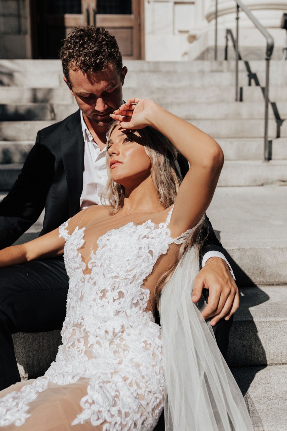 Intimate wedding moment captured in sunlight on grand stone staircase.