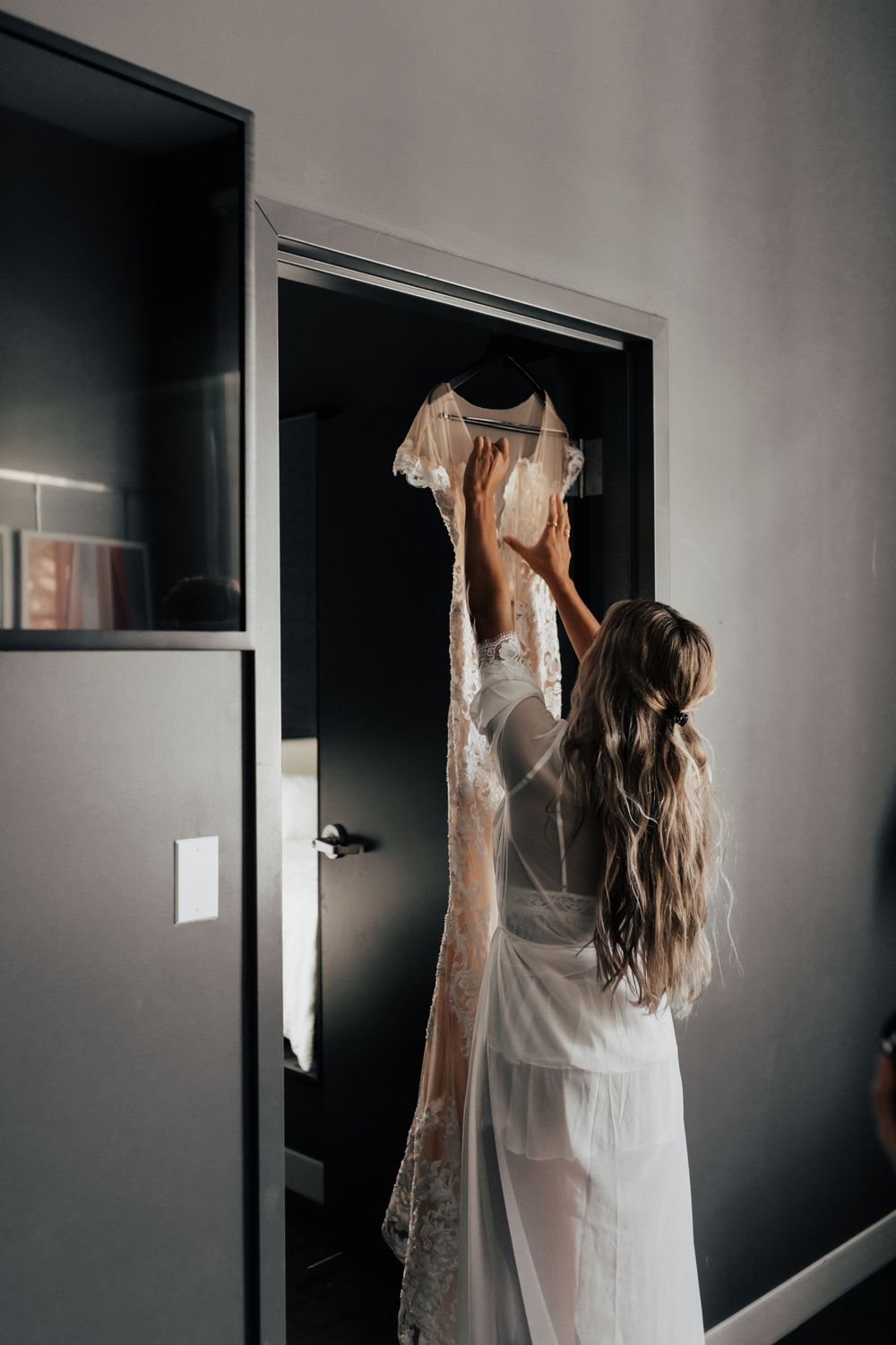 A flowing white wedding gown hangs gracefully on display against a dark door.