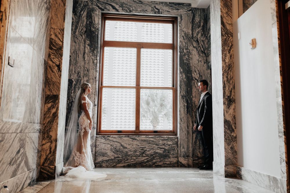 A romantic wedding photography session in an elegant marble-walled room with large windows.
