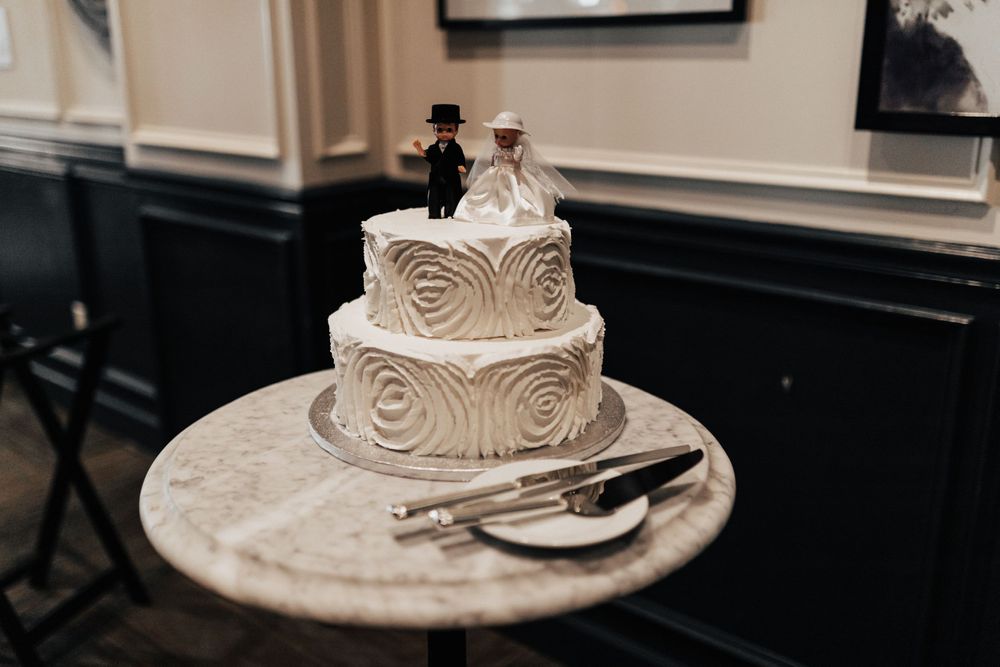 Three-tiered white wedding cake with swirled design and cutting utensils on marble table.