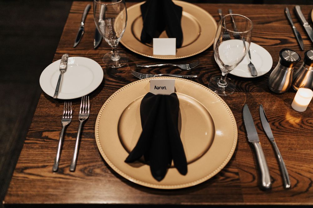 Elegant place setting with black napkin and gold charger plate on wooden table at formal dinner event.