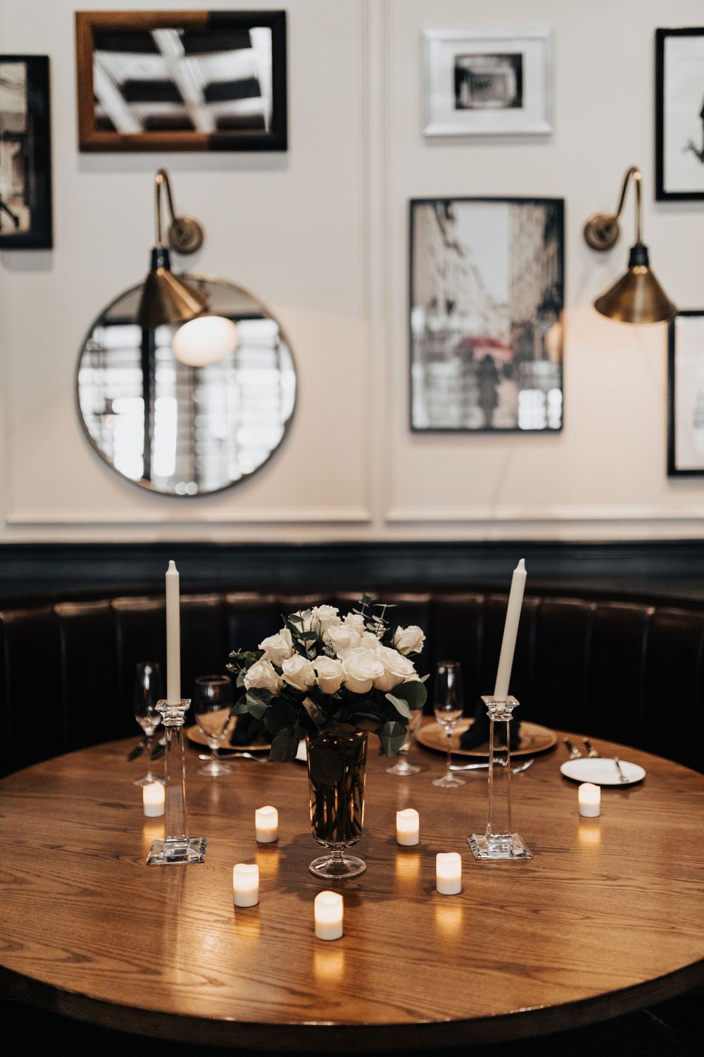 Romantic table setting with white flowers, candles and round mirror on wall in restaurant.