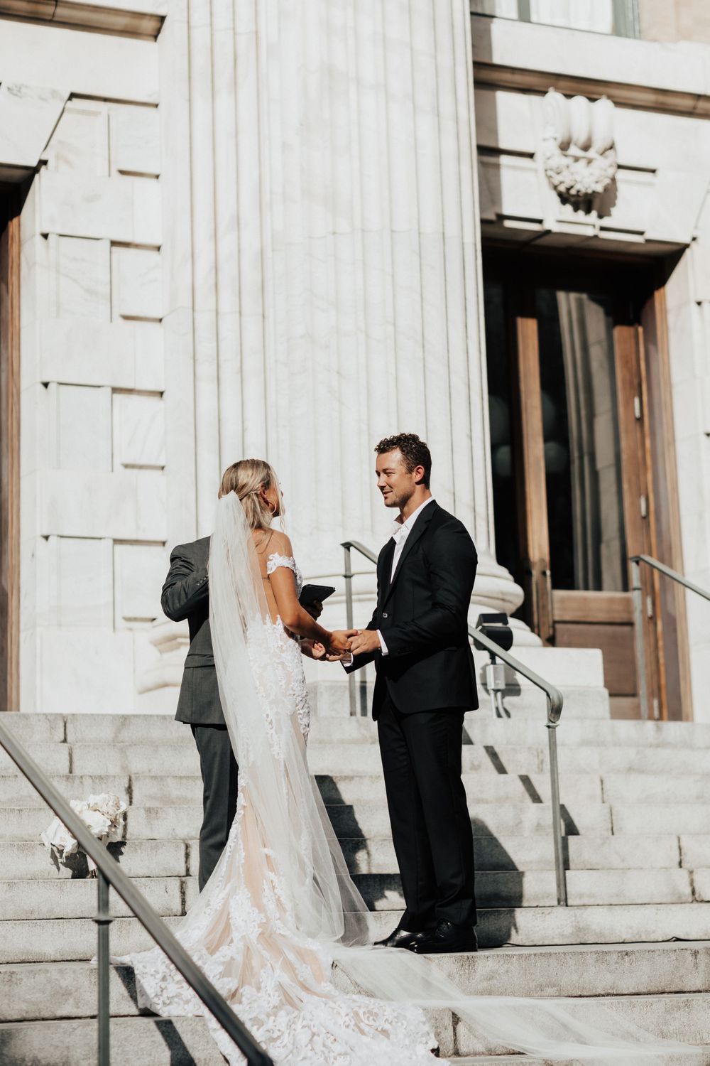 Wedding ceremony taking place on stone steps of historic building with columns.