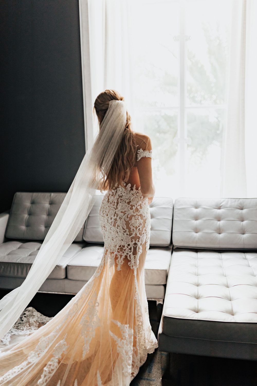 An intricate lace wedding gown with flowing train and veil photographed against natural light.
