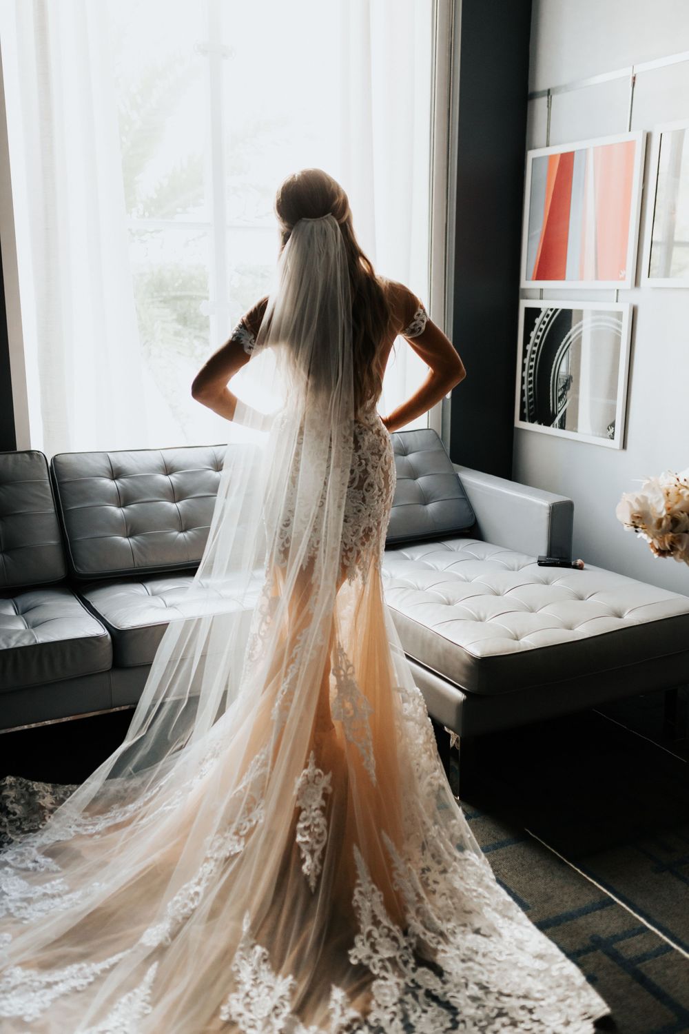 A dramatic silhouette of a wedding dress with cathedral veil against bright window light.