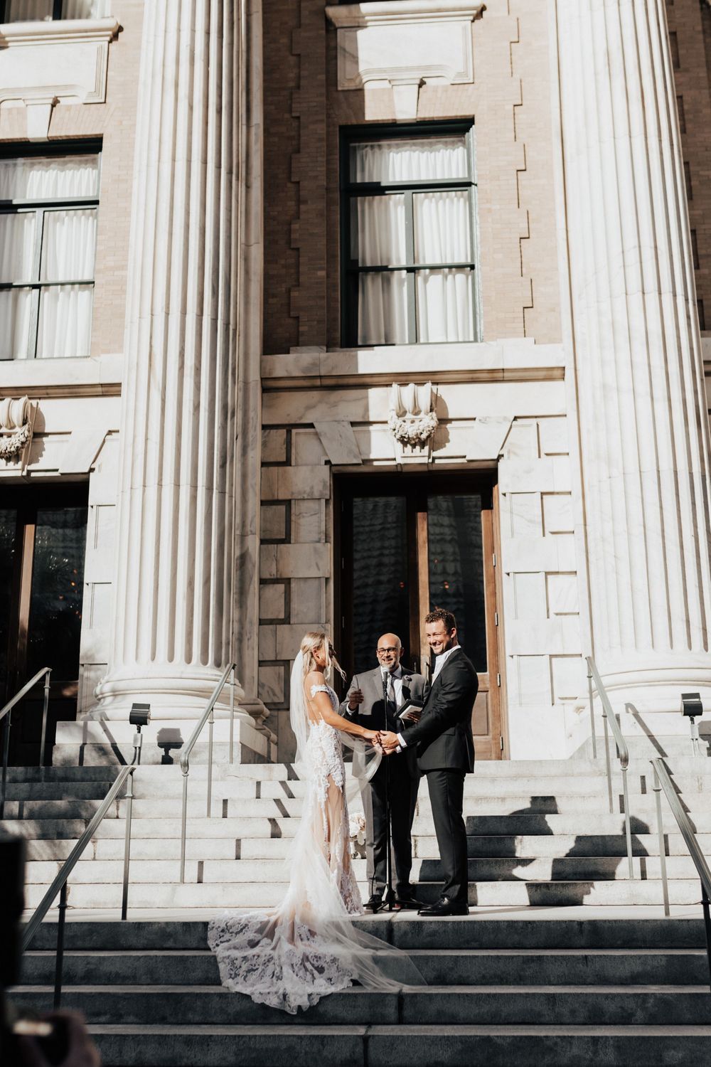 A wedding ceremony taking place on grand stone steps with white columns of a historic building.