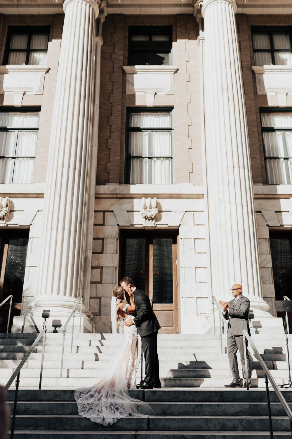 A couple shares an intimate moment during their wedding on the steps of a neoclassical building.